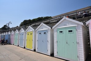 A row of colorful beach huts with numbered doors, a staircase leading to a viewing platform, and a clear sky. - High Cliff Orchard (Lyme Regis)