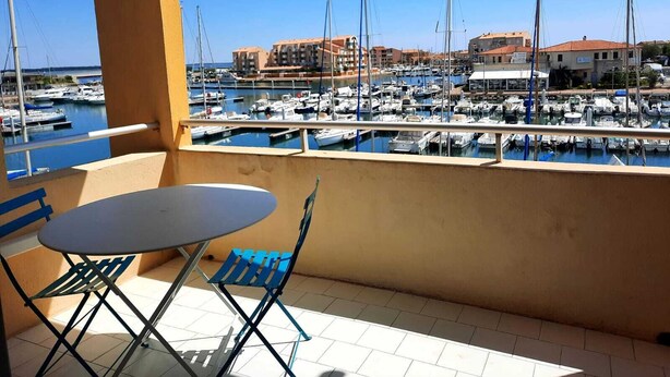 Een balkon met een tafel en stoelen met uitzicht op een jachthaven, met boten en gebouwen op de achtergrond.