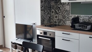 Een moderne keuken met witte kasten, een zwart-wit betegelde spatwand, een ingebouwde oven en een eethoek met een witte tafel en zwarte stoelen.
