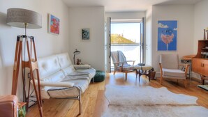 A modern living room with a white sofa, a wooden floor, and a large window. - Lyme Time (Lyme Regis)