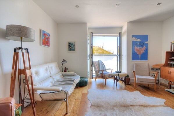 A modern living room with a white sofa, a wooden floor, and a large window. - Lyme Time (Lyme Regis)