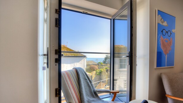 A balcony with a chair, a small table with headphones, and a view of the sea and buildings. - Lyme Time (Lyme Regis)