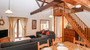 A cozy living room with a wooden staircase, a sofa set, a dining table set for two, and a television. - 3 Home Farm South (Lyme Regis)