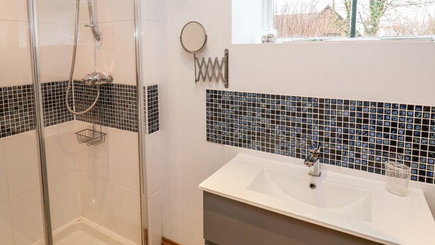 A bathroom with a glass shower enclosure, a white sink, and a window with a view of trees. - 3 Home Farm South (Lyme Regis)