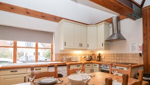 A modern kitchen with white cabinets, wooden beams, a large window, and a dining table set for four. - 3 Home Farm South (Lyme Regis)