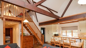 A spacious living area with a staircase, wooden beams, a dining table, and a kitchen area. - 3 Home Farm South (Lyme Regis)