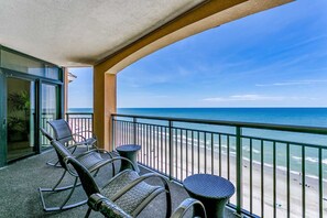 Enjoy the ocean view from this balcony with comfortable seating and a door leading to the interior.