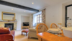 A cozy living room with a fireplace, a television, a dining table with chairs, and a large mirror above the fireplace. - Foxley Cottage (Bridport)