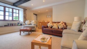 A cozy living room with a sofa, a chair, a coffee table, and a bookshelf. - Foxley Cottage (Bridport)