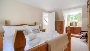 A bedroom with a wooden bed, a dresser, a mirror, and a window with curtains. - Foxley Cottage (Bridport)