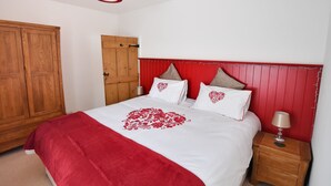 A bedroom with a wooden wardrobe, a bed with a red heart design, and a nightstand with a lamp. - Sunnyside (Colyton)