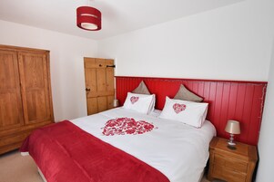 Un dormitorio con un armario de madera, una cama con diseño de corazón rojo y una mesita de noche con lámpara.