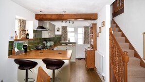 A kitchen with a wooden island, bar stools, a staircase, and a view to the living area. - Sunnyside (Colyton)