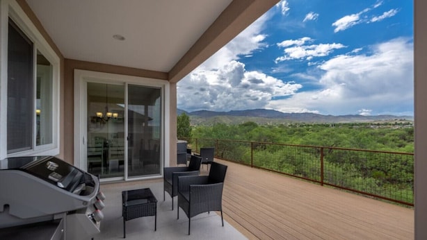 Un balcón con una parrilla, sillas y vistas a un paisaje montañoso.