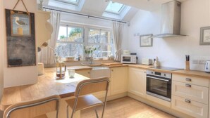 A modern kitchen with a skylight, wooden cabinets, a built-in oven, and a dining area with chairs. - Bethel Cottage (Lyme Regis)