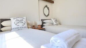 A hotel room with two beds, each with a white comforter and pillows, a wooden nightstand with a lamp, and a mirror on the wall. - Bethel Cottage (Lyme Regis)