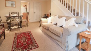 A living room with a beige sofa, a red patterned rug, a dining table with chairs, and a staircase with white railings. - 44 Fernhill Heights (Bridport)
