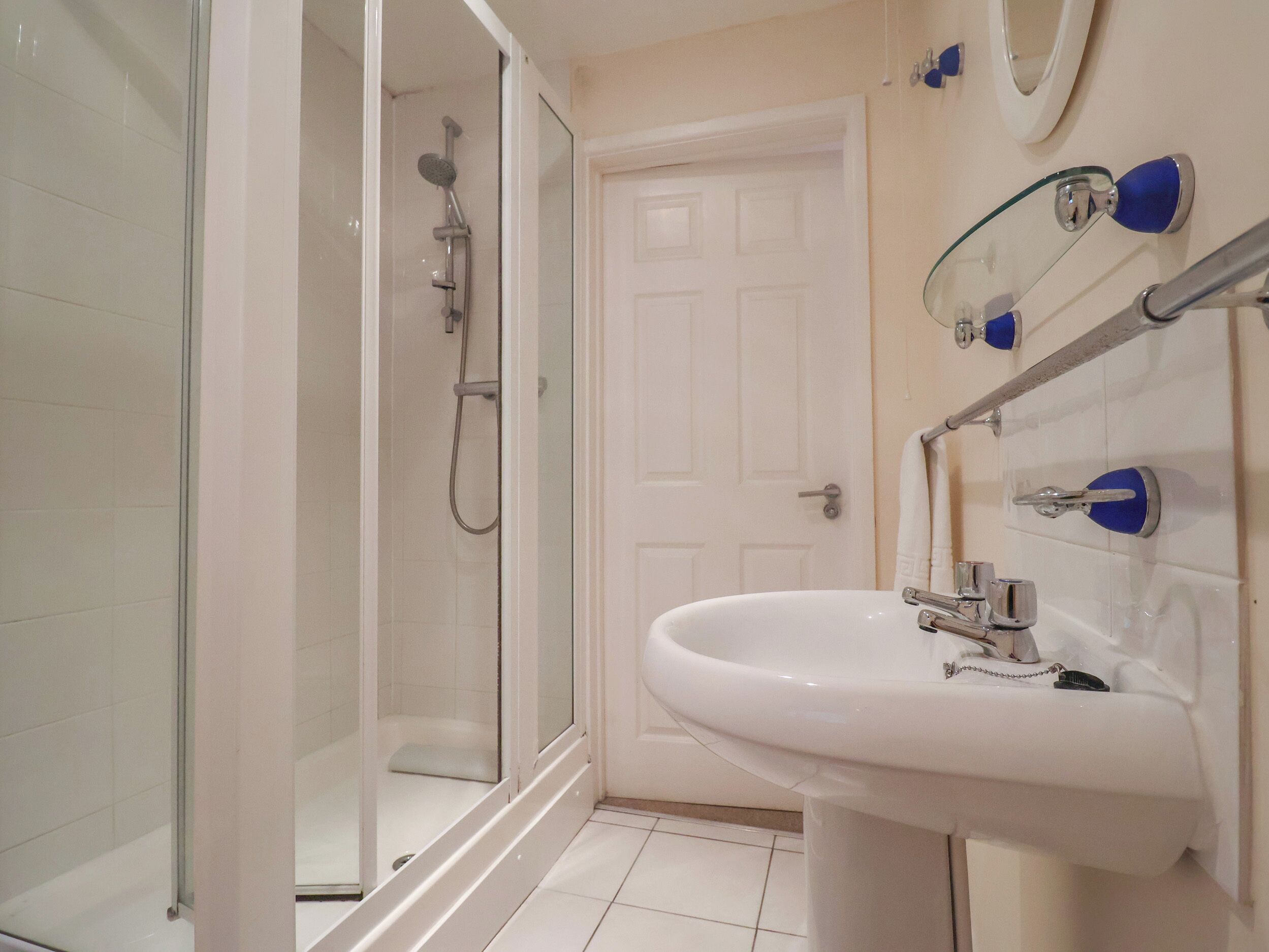 Un bagno con doccia vetro, lavandino bianco e una porta.
