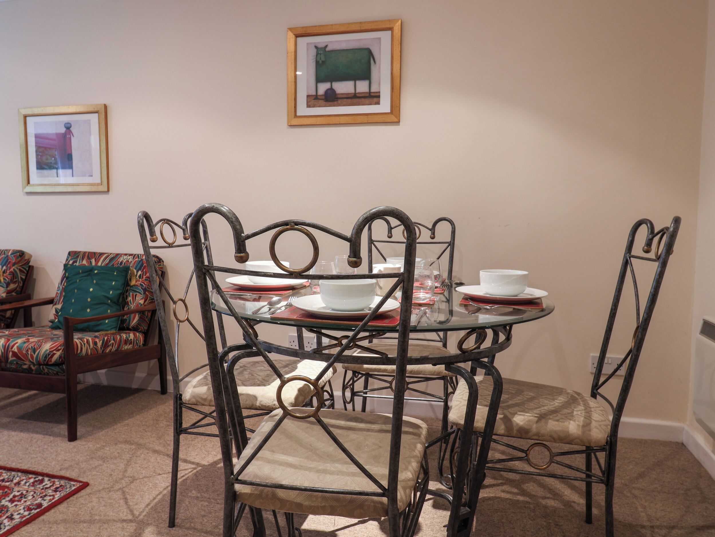 Un comedor con una mesa redonda de vidrio, sillas de metal y una alfombra estampada.