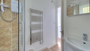 Een badkamer met een douchecabine van glas, een inbouw handdoekhouder, een witte wastafel en een spiegel.