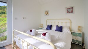 Een slaapkamer met een bed, nachtkastjes en een raam met uitzicht op groen.