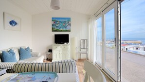 Een kamer met een groot raam, een televisie, een schilderij en een gestreepte bank.