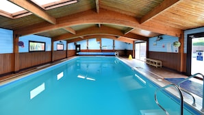 An indoor swimming pool with wooden beams, a bench, and safety signs. - 4 Pinewood Retreat (Axminster)