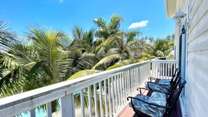 A balcony with a white railing, a pool, and palm trees.