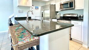 A modern kitchen with white cabinets, stainless steel appliances, and a bar stool with a colorful floral seat.