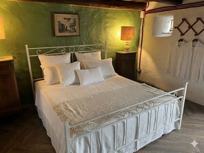 Un letto rifatto con lenzuola e cuscini bianchi, una parete verde, un quadro incorniciato e una lampada a parete.