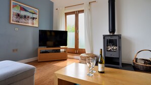 Ett vardagsrum med en tv, ett träbord med glas och en flaska, en öppen spis och en tavla på väggen.