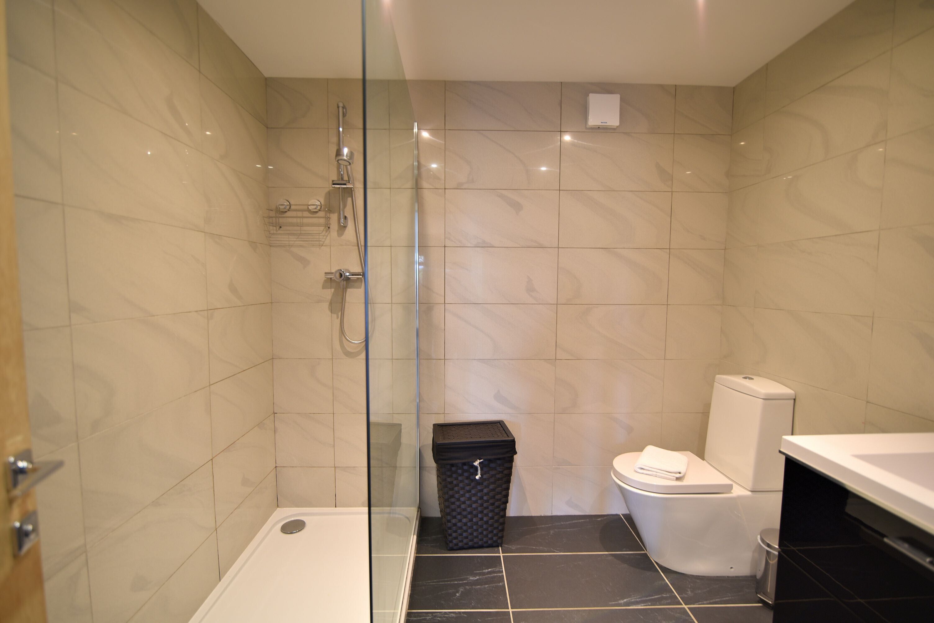 A modern bathroom with a glass-enclosed shower, a white toilet, and a black trash bin.
