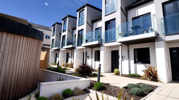 A row of modern, two-story residential buildings with balconies, a landscaped garden area, and a clear blue sky. - 3 Grove Mews (Seaton)