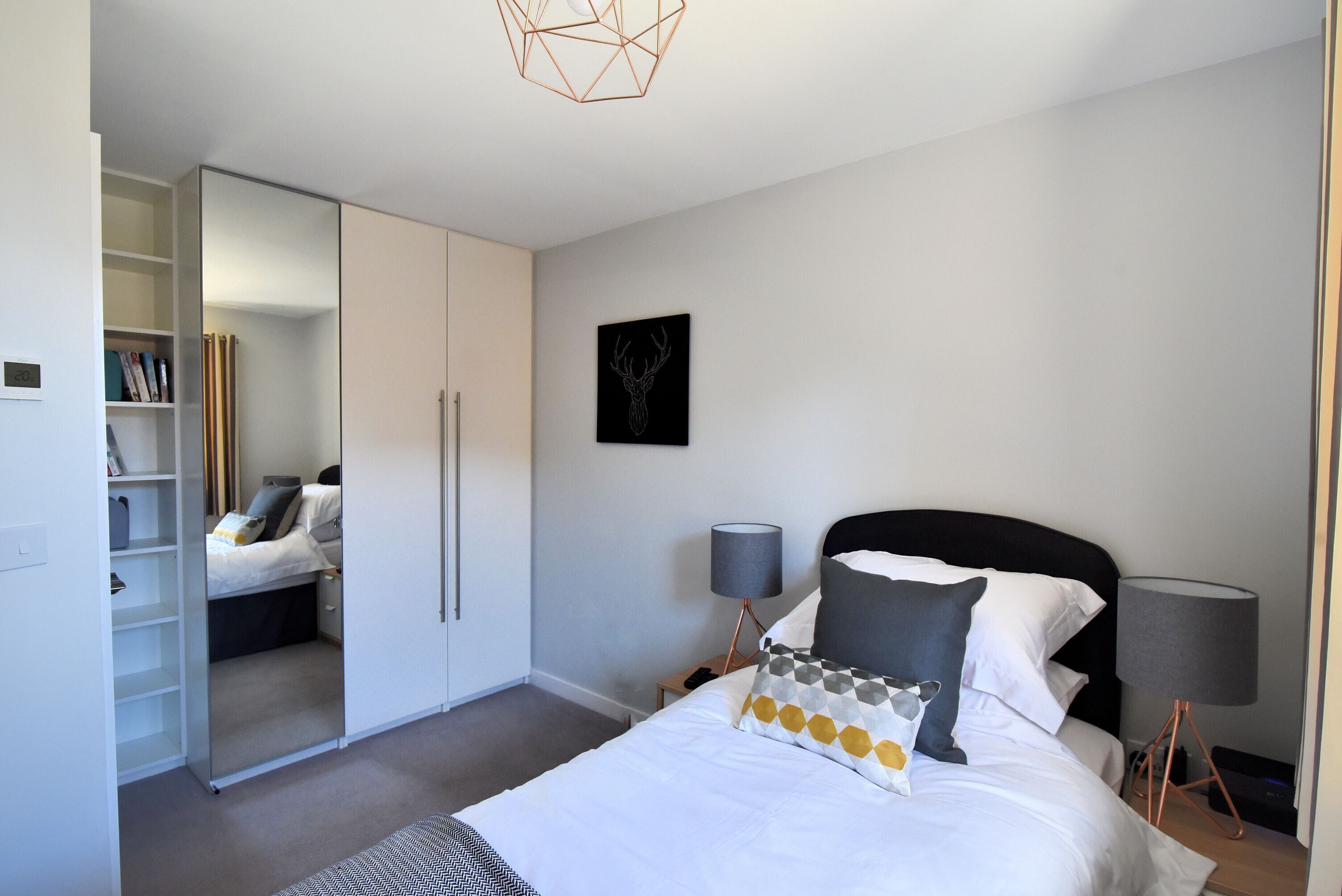 Een slaapkamer met een bed, nachtlampjes, een kledingkast en een lijst aan de muur.