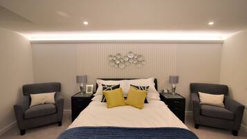 Quarto com uma cama grande, duas mesas de cabeceira, duas poltronas e um objeto decorativo na parede.