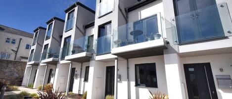A modern residential building with multiple balconies, large windows, and a well-maintained garden area.