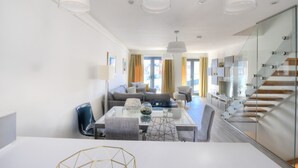 A modern living room with a glass dining table, a sofa, and a staircase with glass railings. - 3 Grove Mews (Seaton)