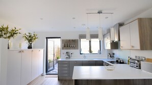 A modern kitchen with white cabinets, a large island, pendant lights, and a view to the outside. - 3 Grove Mews (Seaton)