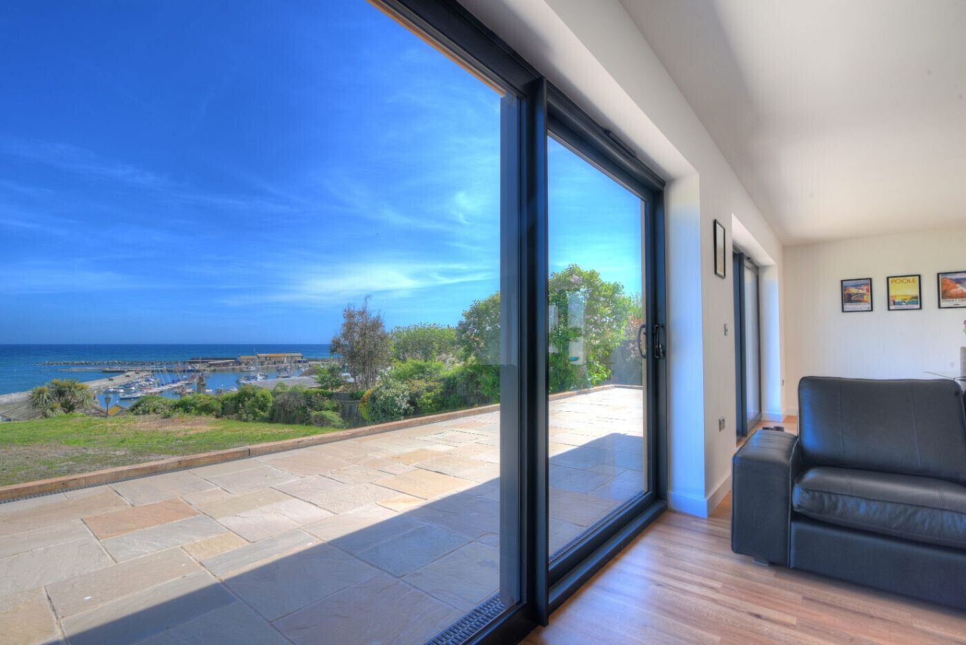 Una sala de estar moderna con un amplio ventanal corredera que da a un balcón con vistas al mar y a barcos.