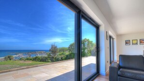 A modern living room with a large sliding glass door leading to a balcony with a view of the sea and boats. - Harbour Heights Cottage (Lyme Regis)