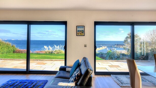 A living room with a large sliding glass door leading to a patio with a view of the sea. - Harbour Heights Cottage (Lyme Regis)