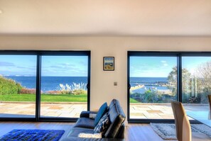 Una sala de estar con un gran ventanal corredera que da a un patio con vistas al mar.
