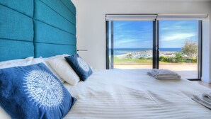 A bedroom with a large bed, a view of the sea, and a sliding glass door. - Harbour Heights Cottage (Lyme Regis)