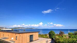 A wooden building with a flat roof overlooking a coastal area with a clear sky and a view of the sea. - Harbour Heights Cottage (Lyme Regis)