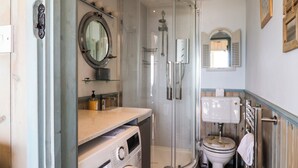 Un baño pequeño con lavadora, cabina de ducha acristalada y retrete.