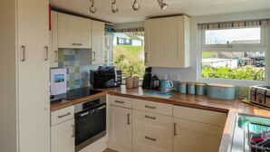Una cocina moderna con armarios blancos, horno integrado, microondas y ventana con vistas al jardín.