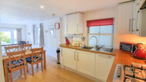 A kitchen with wooden cabinets, a dining table with chairs, a red kettle, a microwave, and a gas stove.