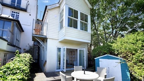 A two-story house with a balcony, a covered patio with wicker furniture, and a shed in the backyard.