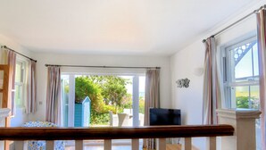 A room with a wooden staircase, a television, and a view of a garden through a glass door.