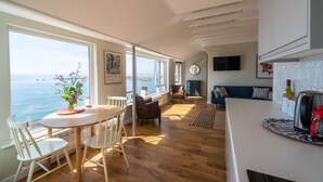 A spacious kitchen with a large window overlooking the sea, wooden flooring, and modern furnishings. - 3 Beach Way House (Lyme Regis)